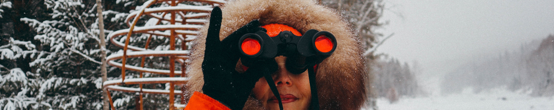 A woman in a winter jacket looking through a pair of binoculars.