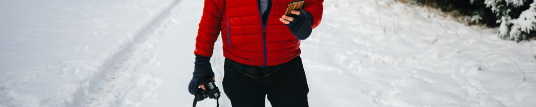 A man holding a camera and a smartphone on a snowy path.