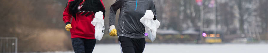 Two people jogging with bags of garbage.