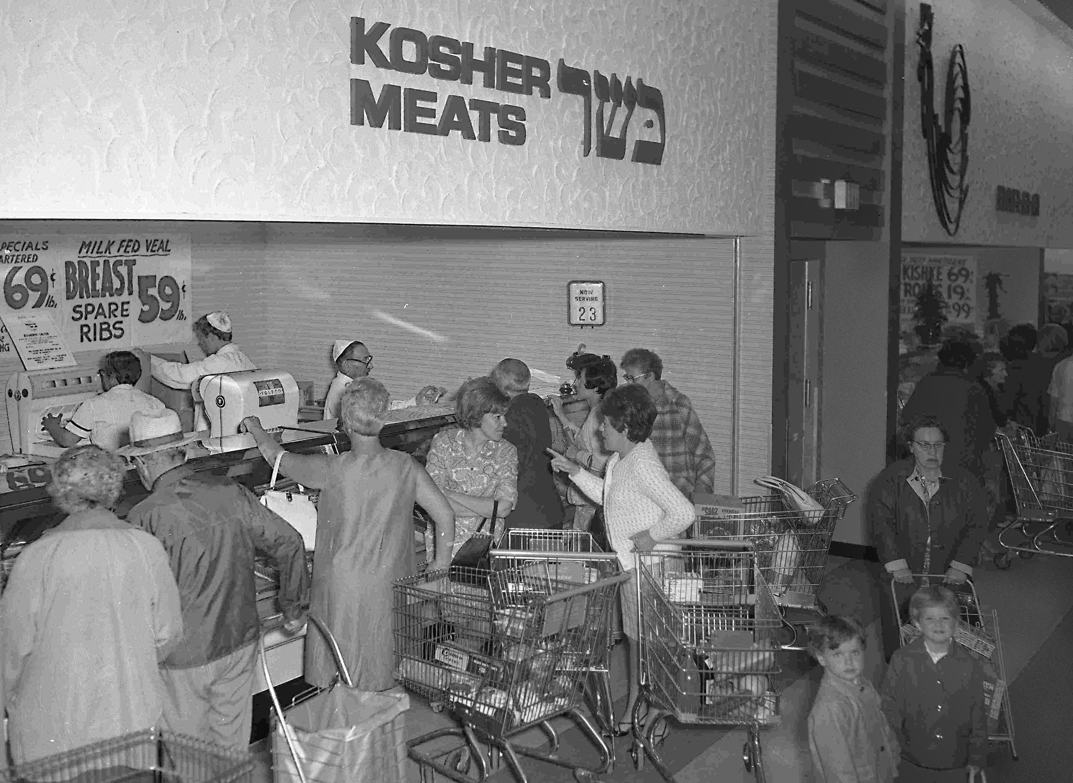 A black and white photo of customers gathered around a kosher deli.