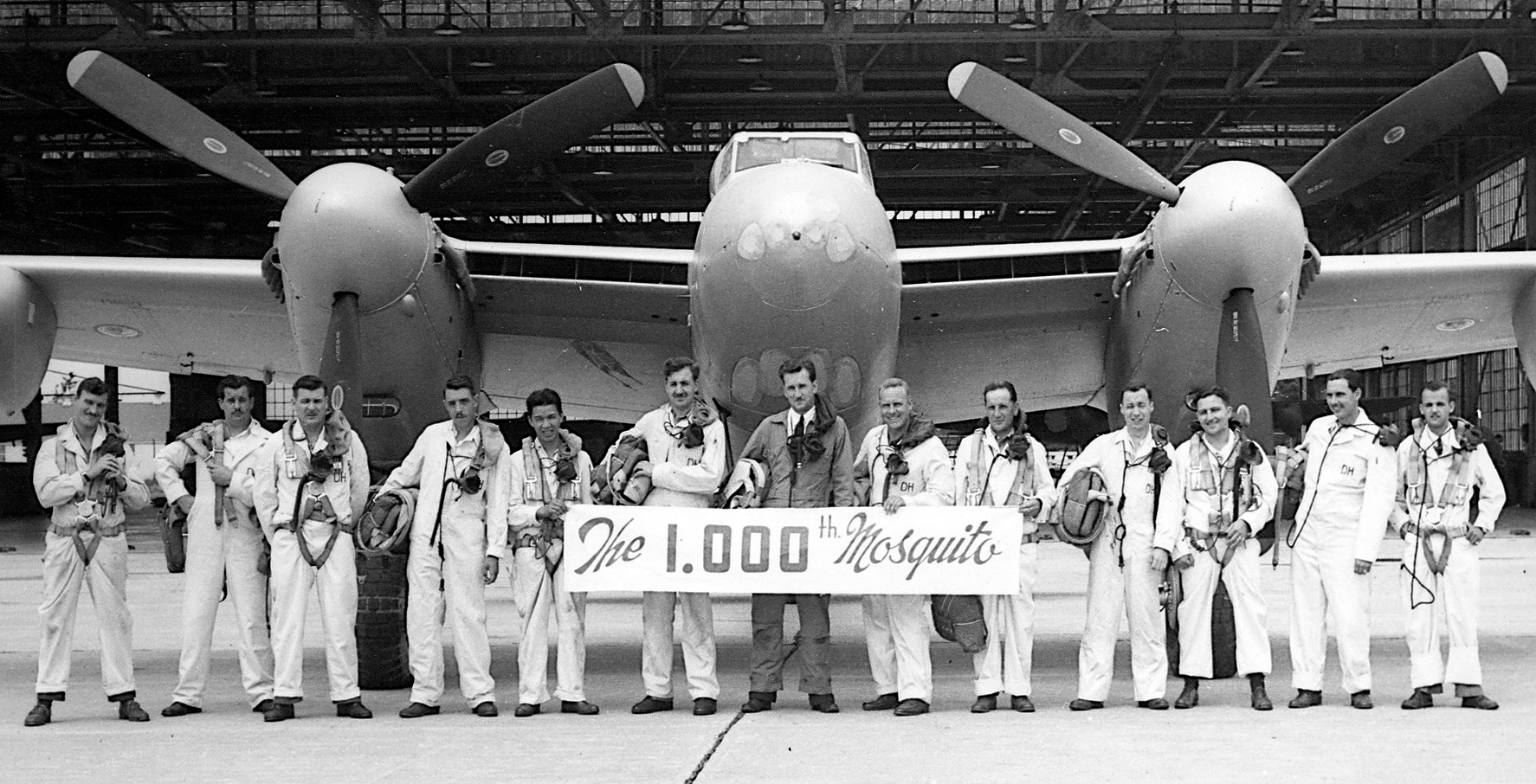 A black and white photo of a line of pilots posing in front of a de Havilland Mosquito aircraft.