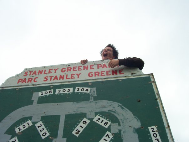 A teenager giving the camera a thumbs-up from behind a large Stanley Greene Park sign.