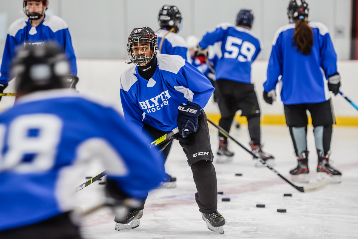 Youth in blue jerseys playing hockey in an arena.