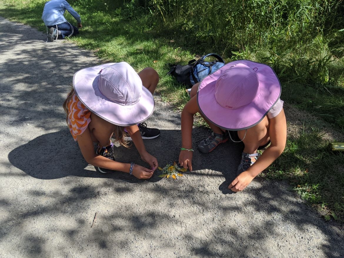Two children in sunhats creating art using leaves and flowers.