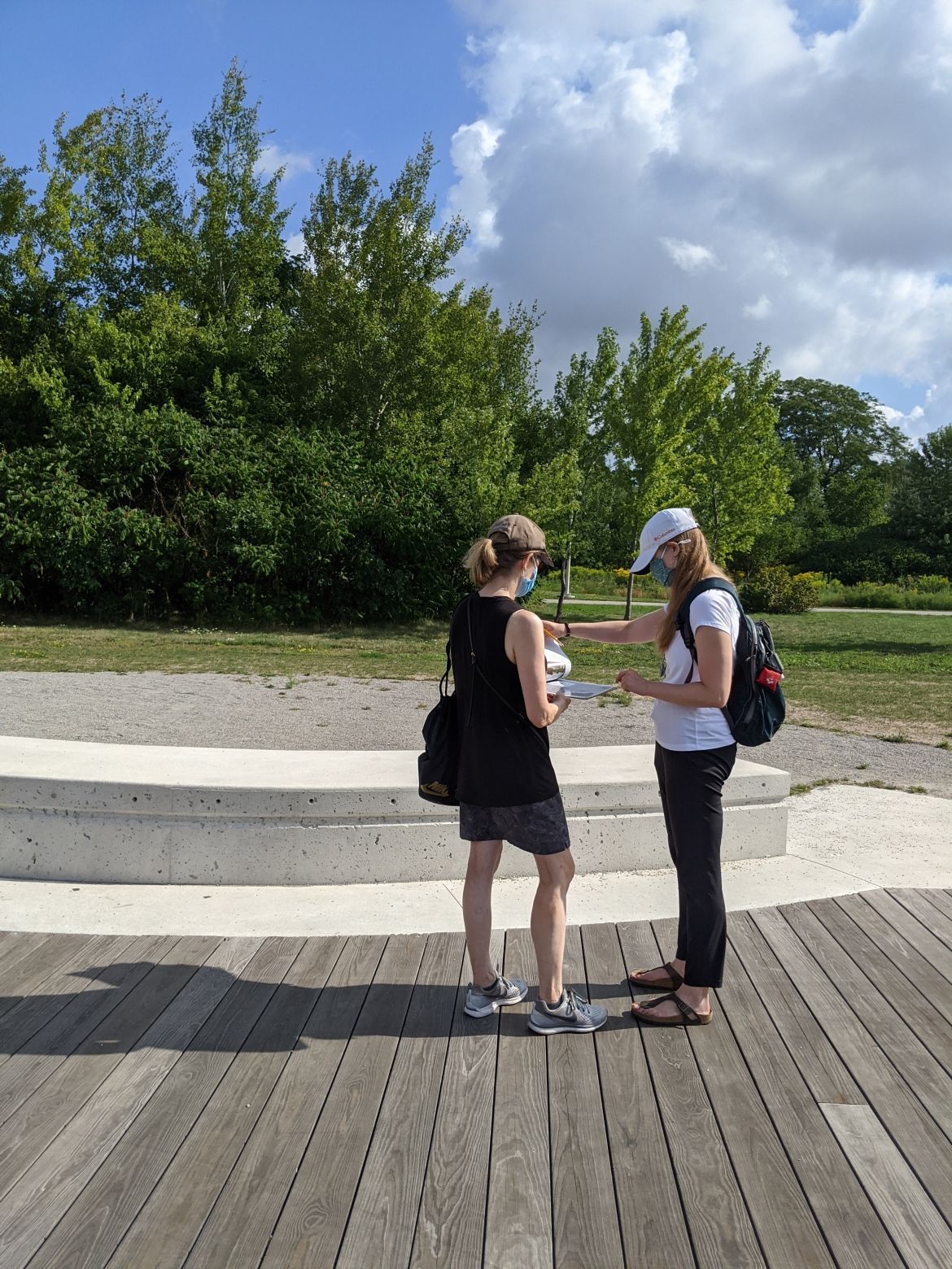 Two adults working on an activity at the park. Trees and a blue sky in the background.