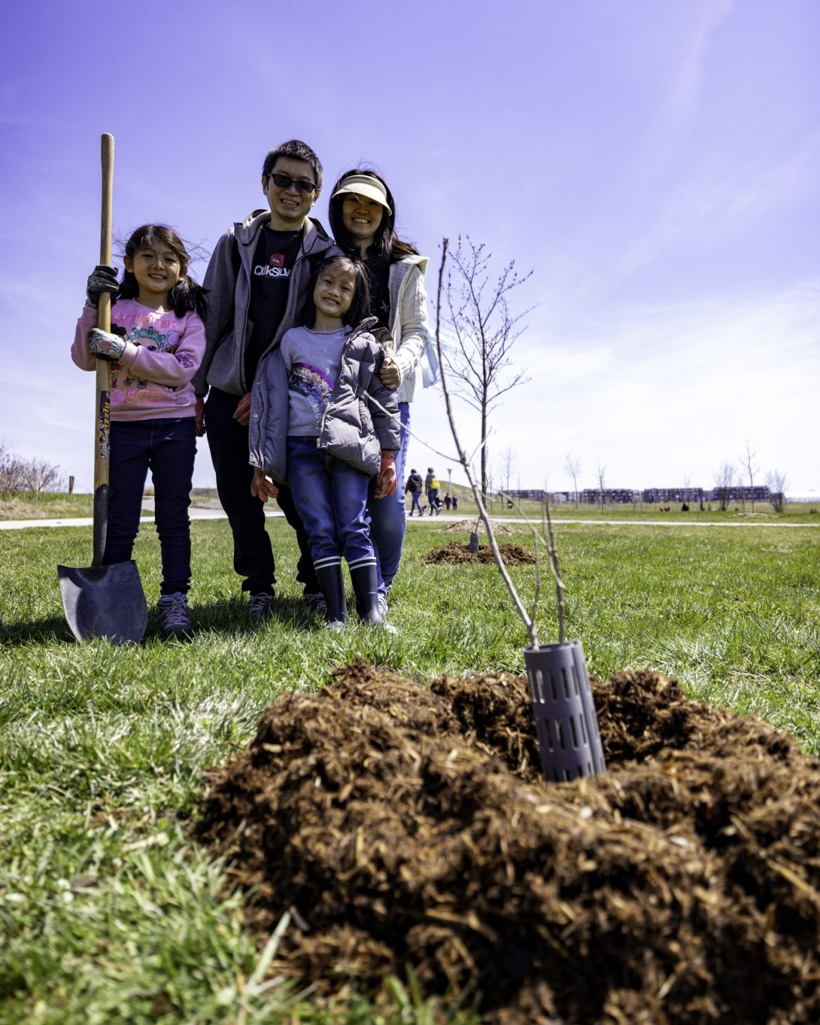A family posing in front of the tree they planted.