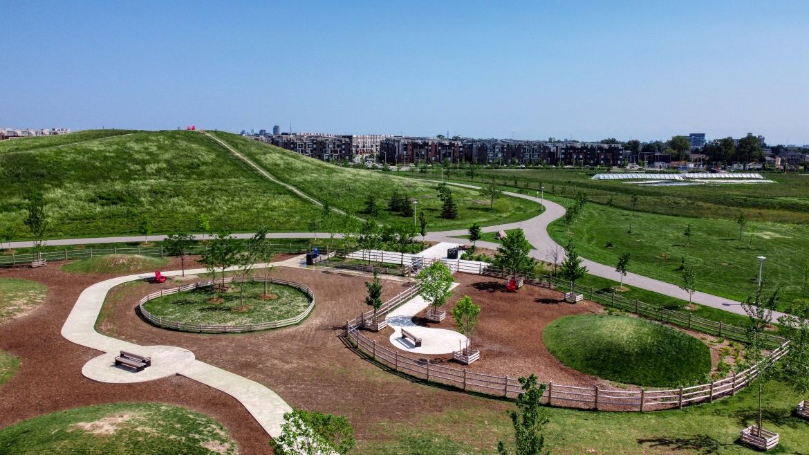 An aerial shot of Dogsview Park. Wooden fencing, grassy mounds, brown mulch, and a paved path.