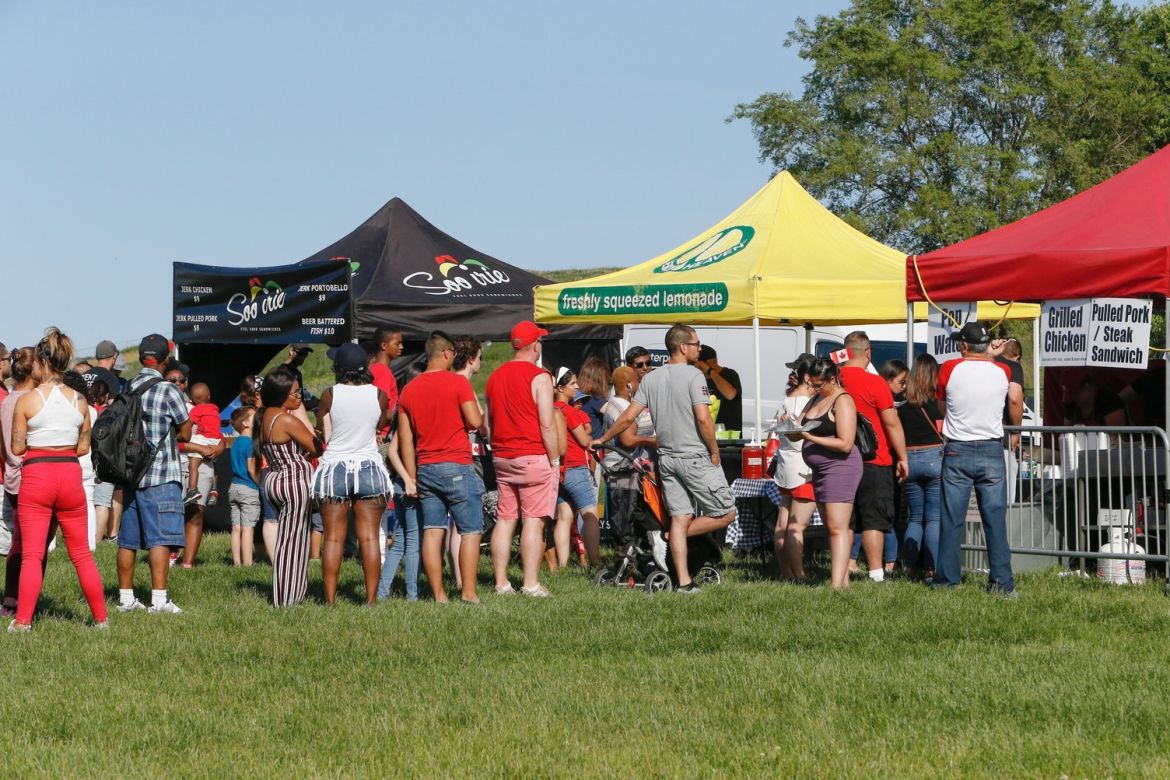 Colour tents set up on a field and people in line for various vendors.