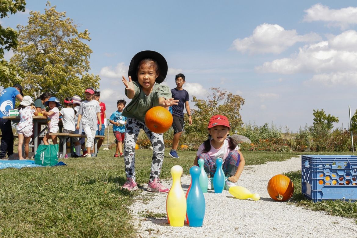Kids using a pumpkin as a bowling ball at the Orchard Party event.