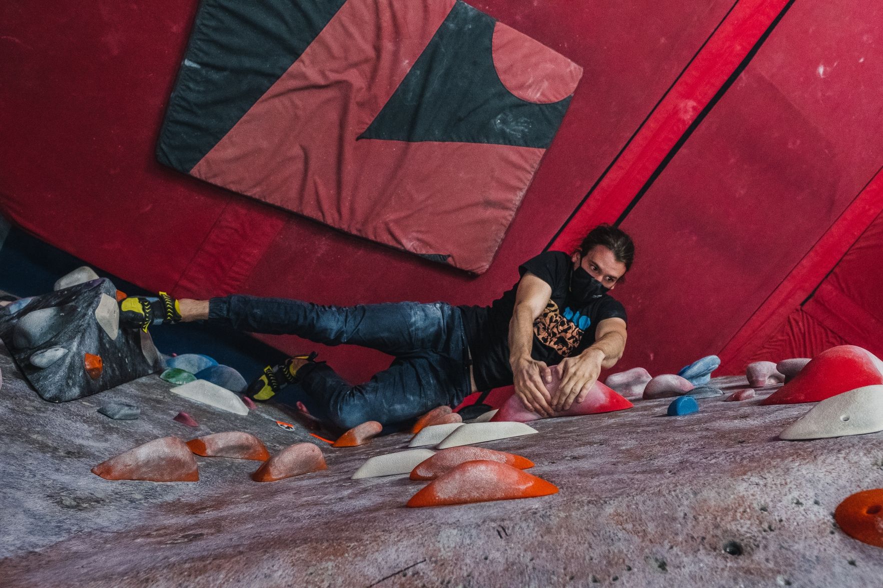 A from-above shot of a climber reaching for colourful holds inside a climbing gym.