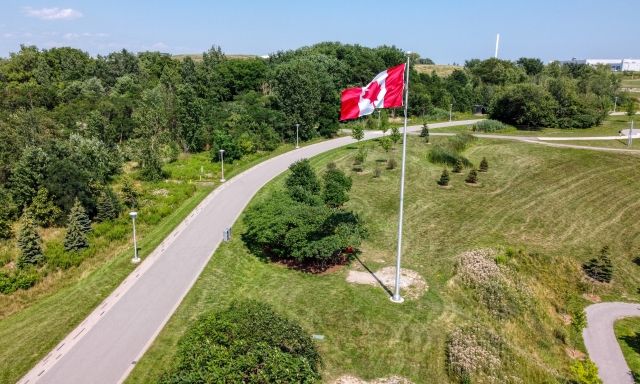 A paved trail, trees, and a Canadian flag.