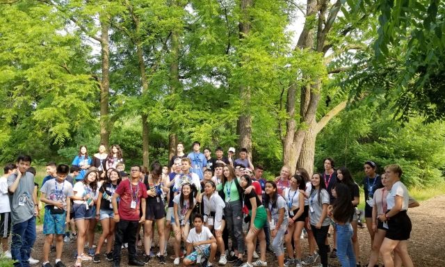 A large group of foreign exchange students standing on a dirt path in a forest.