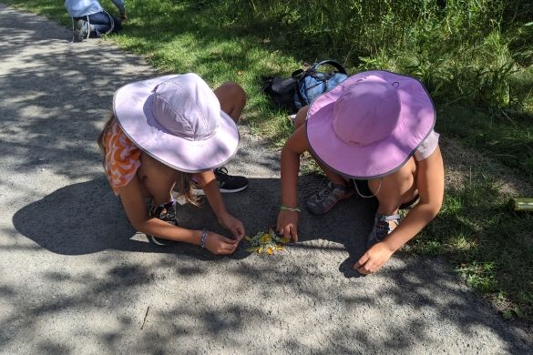 Two children in sunhats creating art using leaves and flowers.