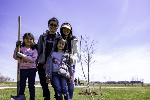 A family posing in front of the tree they planted.