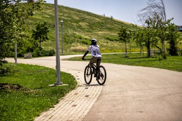 A person on a bike on a paved path, a large green hill in the background.