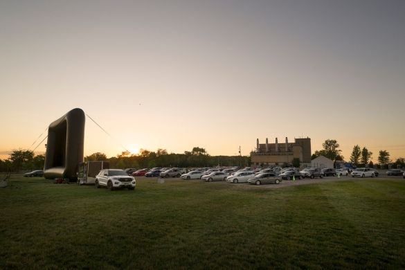 Rows of cars parked in front of an inflatable screen at dusk.
