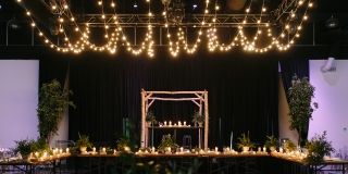 A large table set up with candles and plants in an indoor venue. Fairy lights hanging from the ceiling.