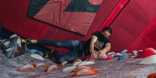 A from-above shot of a climber reaching for colourful holds inside a climbing gym.